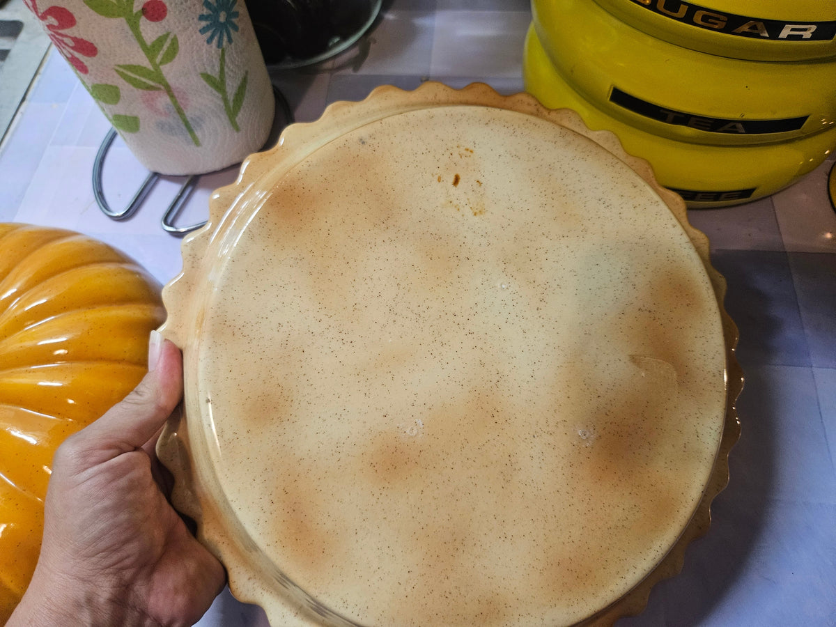 Top view of pie keeper lid exterior showing warm cream speckled glaze and scalloped edge of base beneath