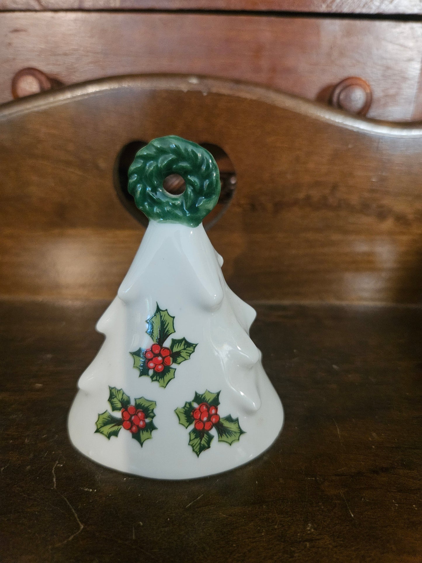 Vintage white ceramic Christmas tree bell with holly berry motif and green sculpted wreath handle, approximately 3 inches tall