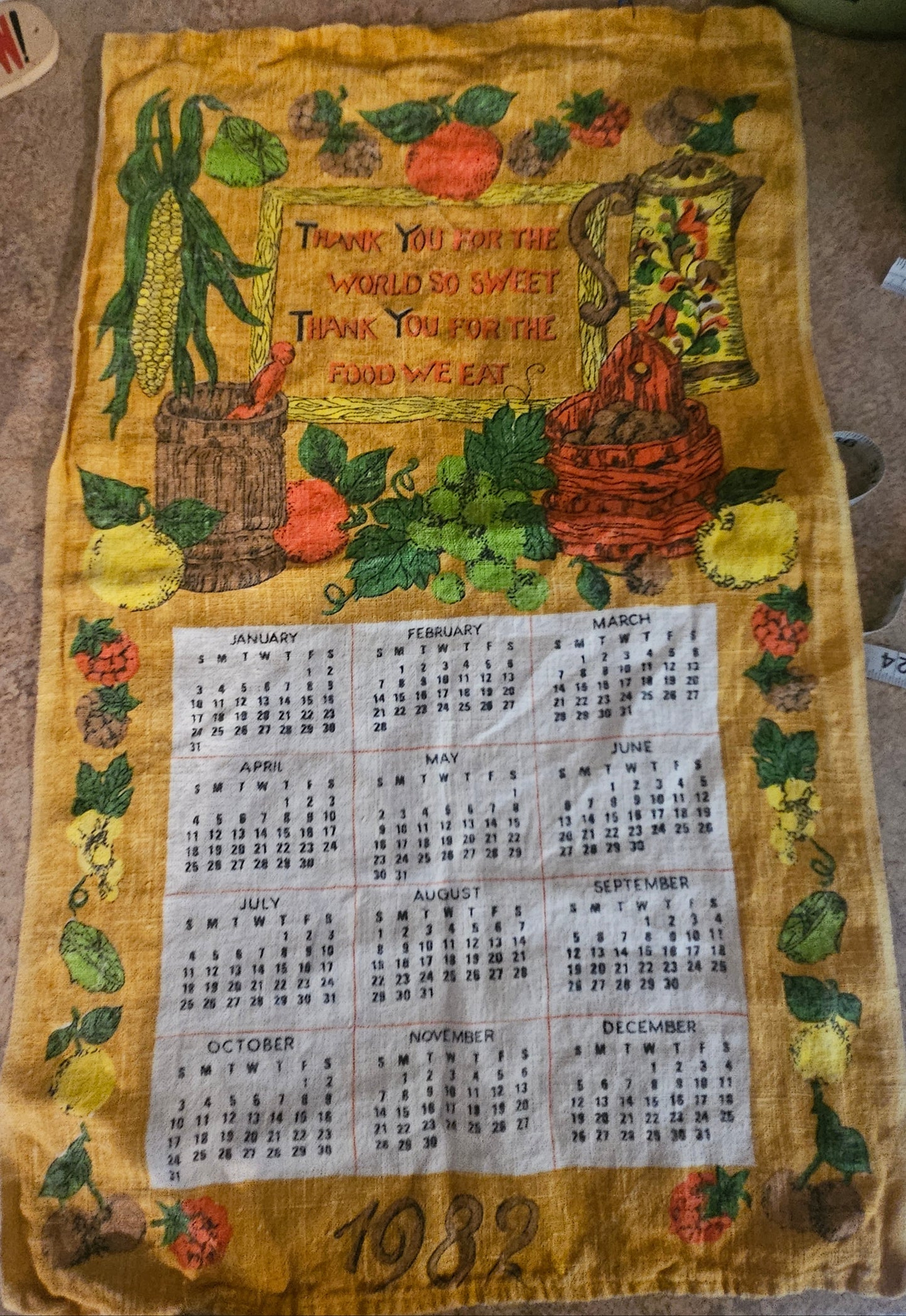 1982 harvest calendar tea towel on golden yellow ground showing corn, squash, crock, basket, and 12-month calendar