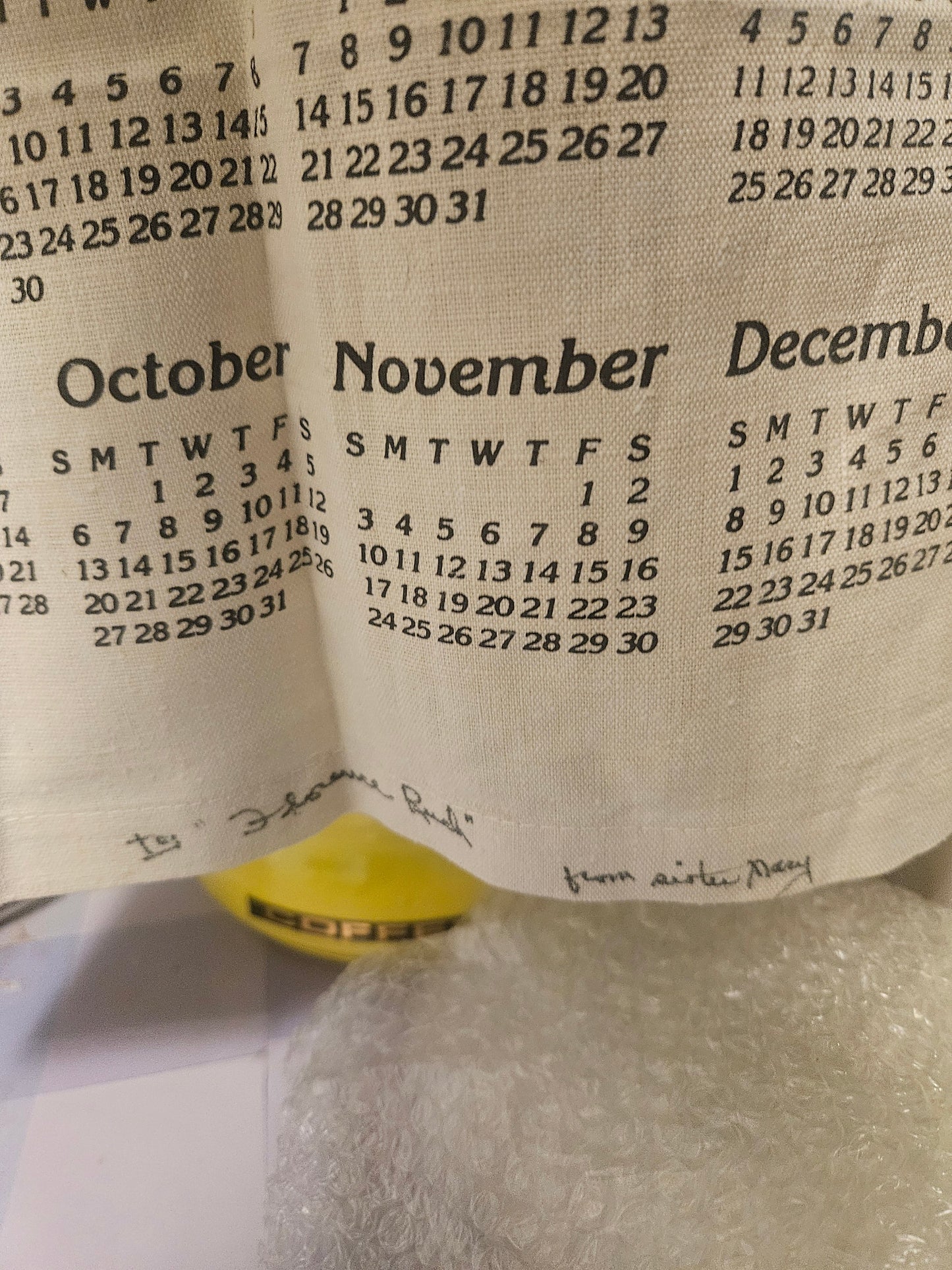 Bottom of 1985 calendar tea towel showing handwritten inscription To Joanne Budi from sister Mary