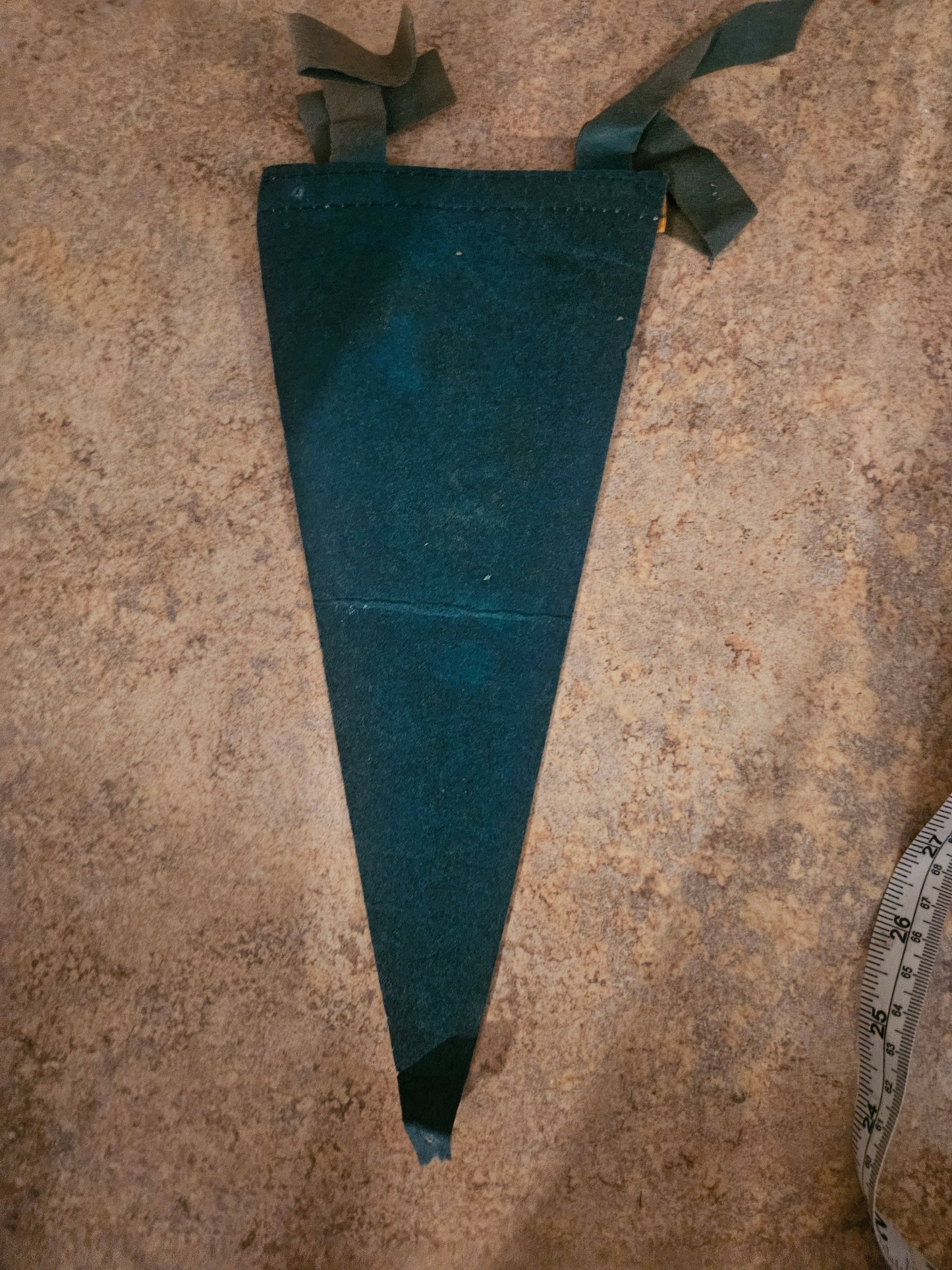Back of vintage Ozarks felt pennant showing green ribbon ties and gold leather trim band with ruler for scale