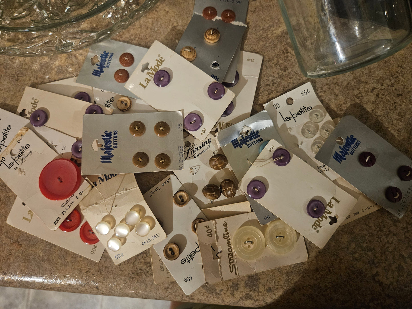 Vintage button cards spread out showing La Mode, Majestic, La Petite, and Streamline brands in purple, red, pearl, and gold