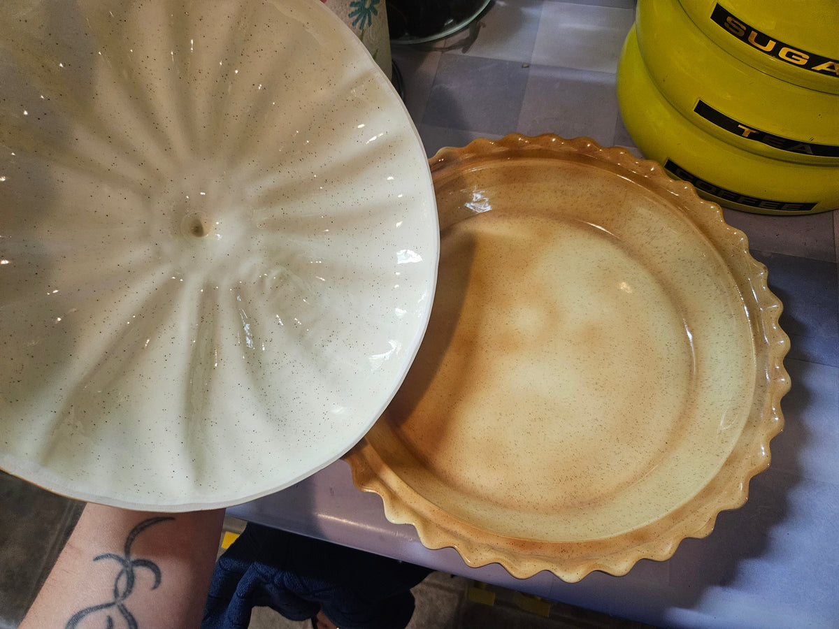 Pie keeper separated showing underside of pumpkin lid with white starburst relief pattern and cream speckled pie dish base