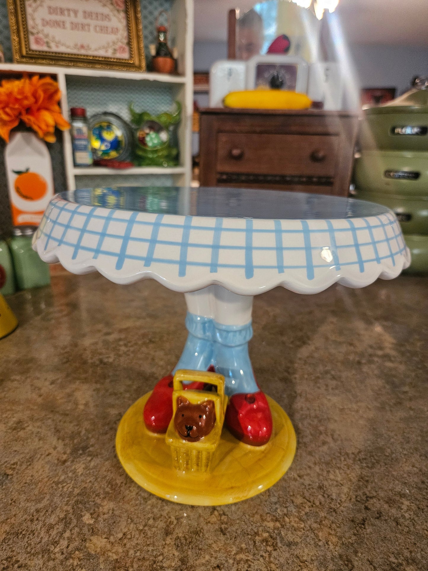 Wizard of Oz Dorothy legs ceramic cake stand front view showing gingham scalloped rim ruby slippers and Toto in basket