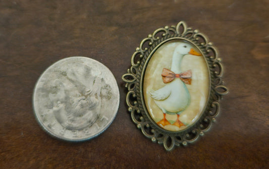 Oval goose brooch with antique brass filigree frame, front view with quarter for scale
