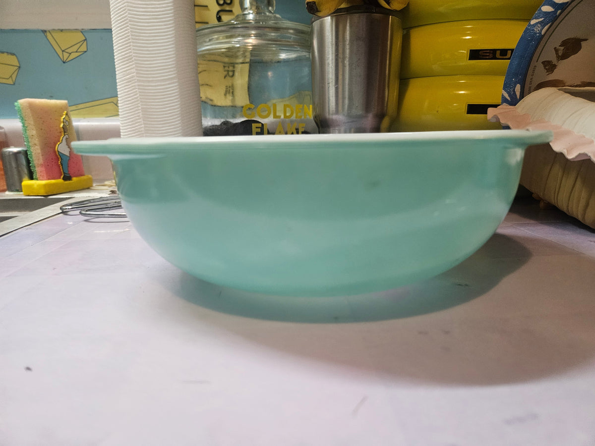 Vintage turquoise glass bowl with white rim, viewed from the side