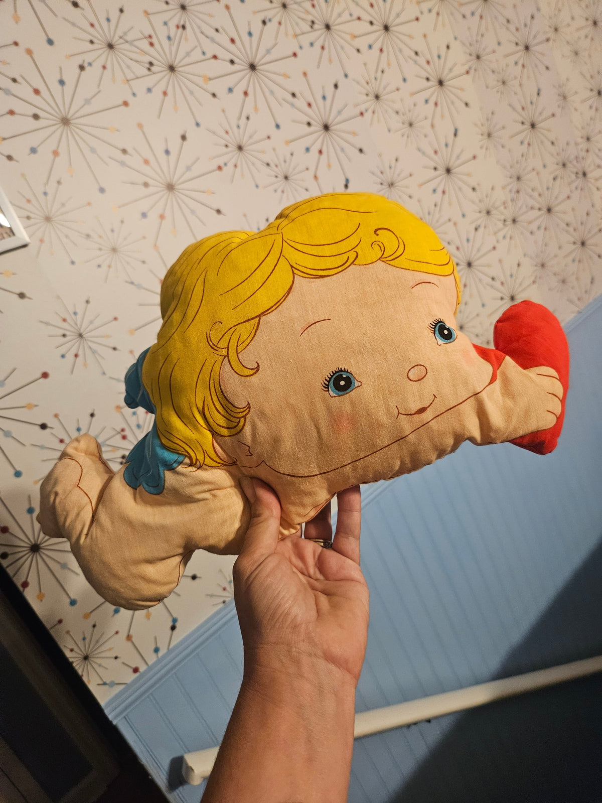 Back of blond baby character-shaped pillow showing yellow hair and red shoes