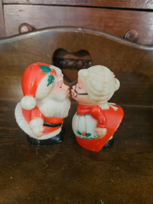 Vintage plastic kissing Santa and Mrs. Claus salt and pepper shakers facing each other on wooden surface
