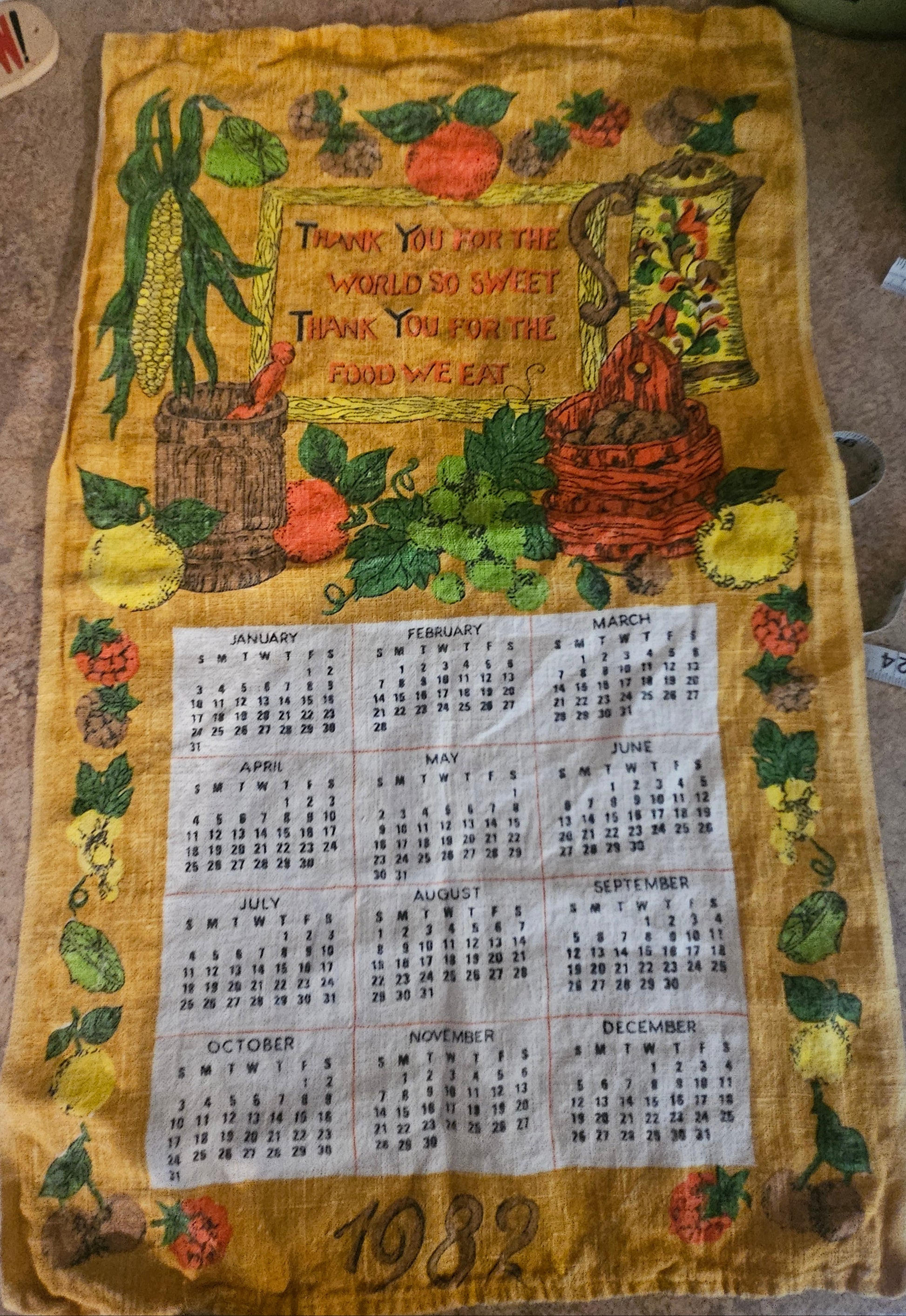 1982 harvest calendar tea towel on golden yellow ground showing corn, squash, crock, basket, and 12-month calendar