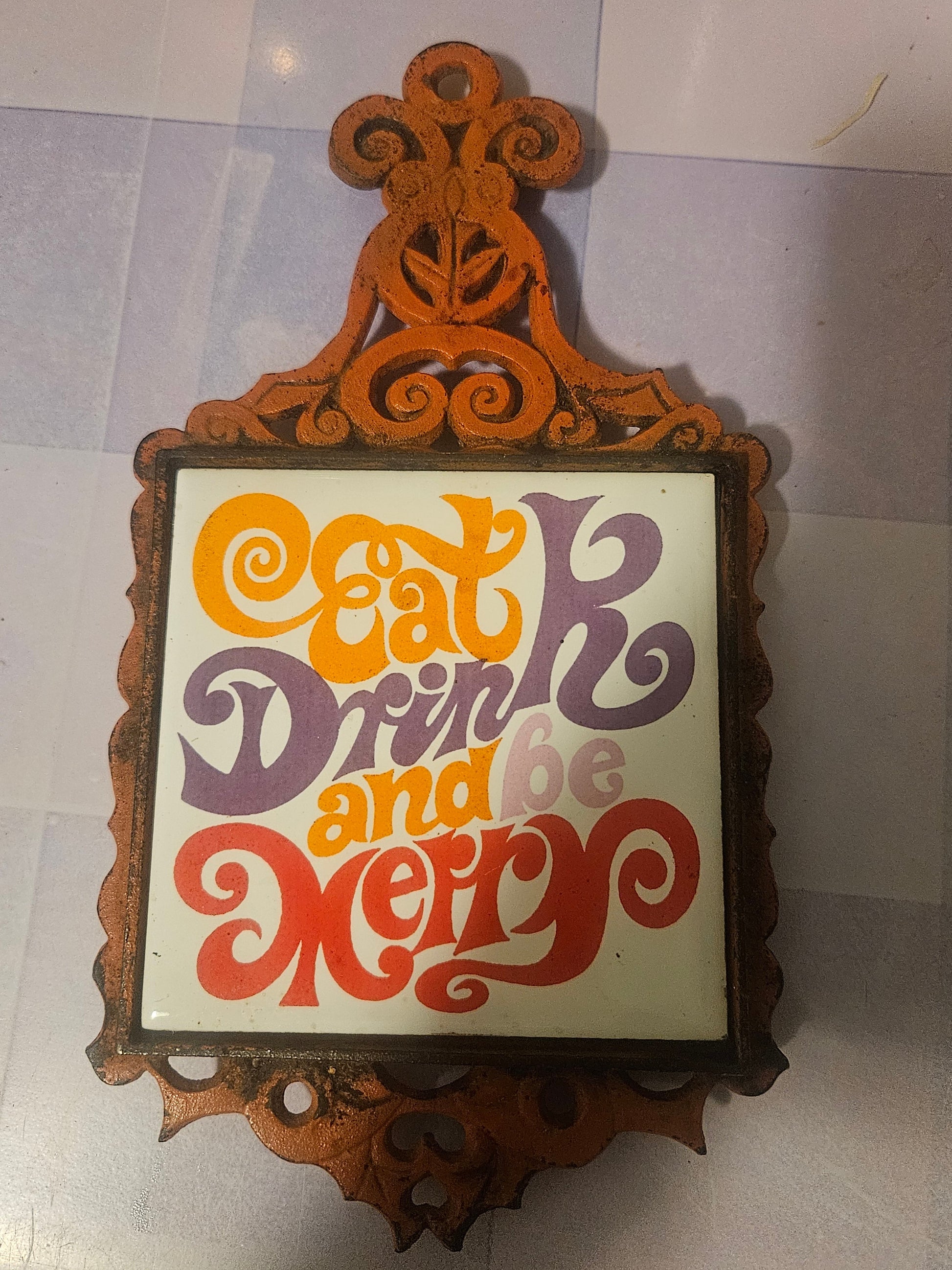 Vintage cast iron trivet with Eat Drink and Be Merry ceramic tile insert in groovy 70s typography