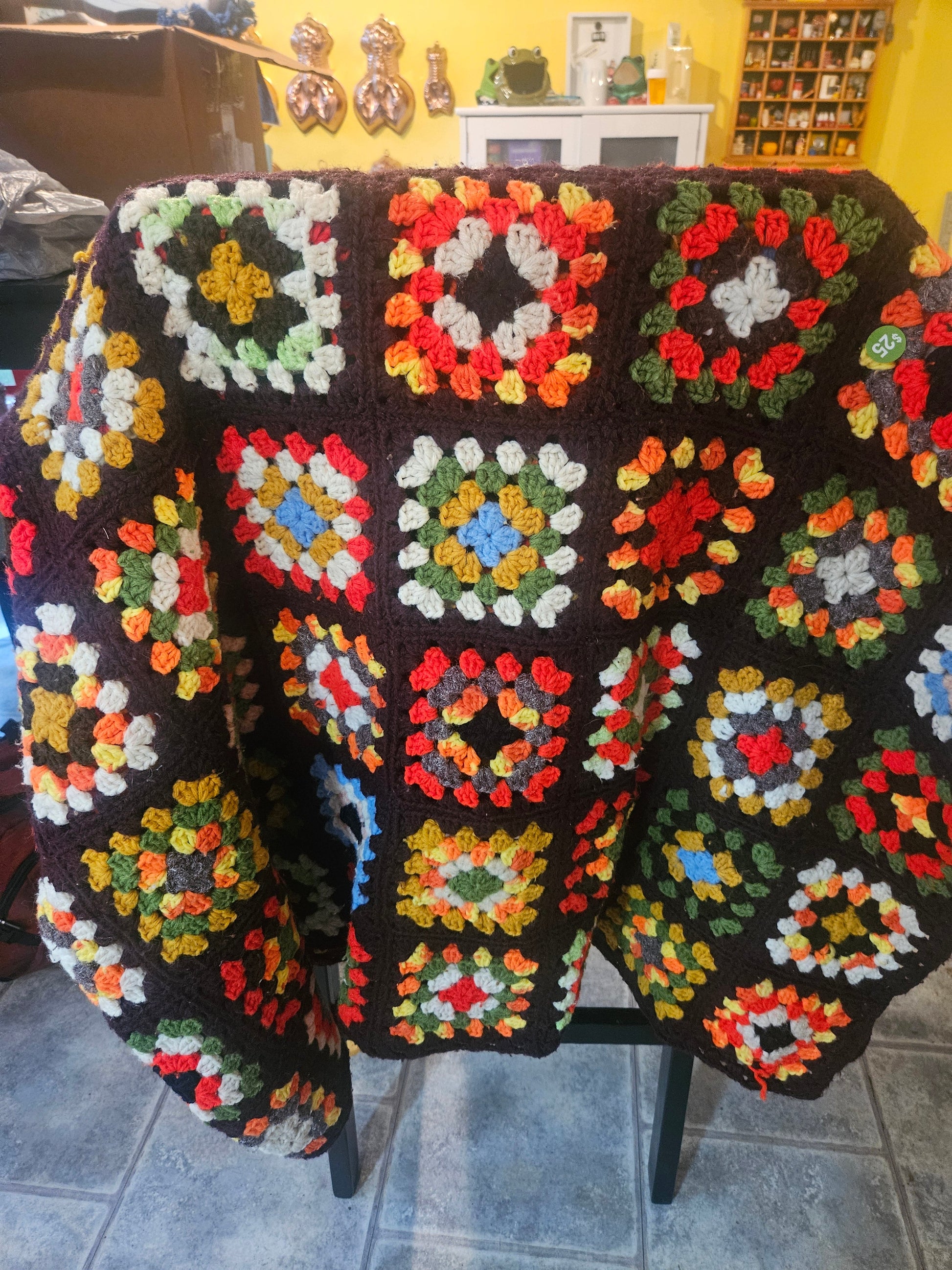 Vintage handmade granny square crochet afghan draped over chair showing dark brown background and multicolor jewel-tone squares