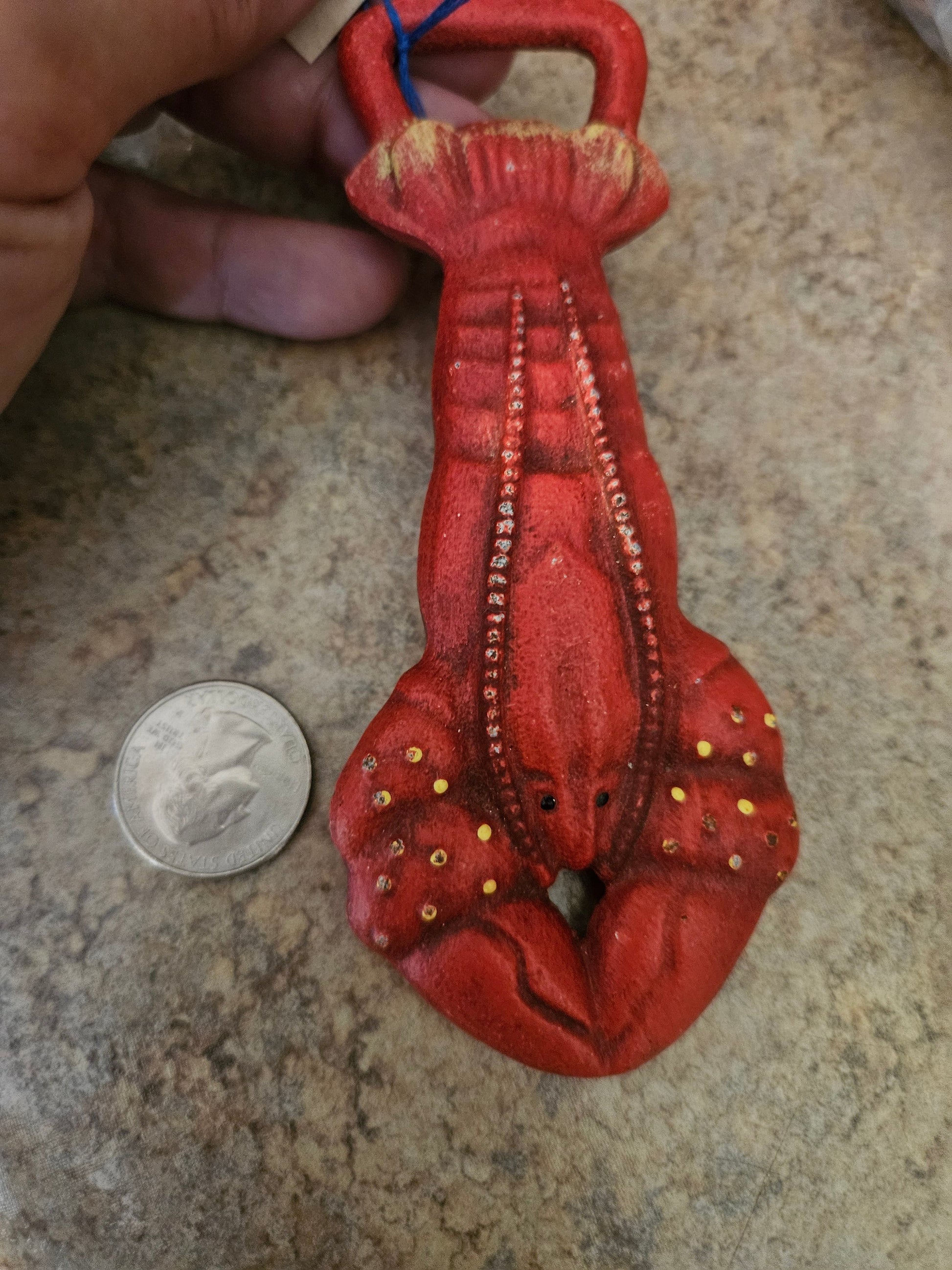 Department 56 cast iron lobster bottle opener in red with gold spot accents, shown with quarter for scale