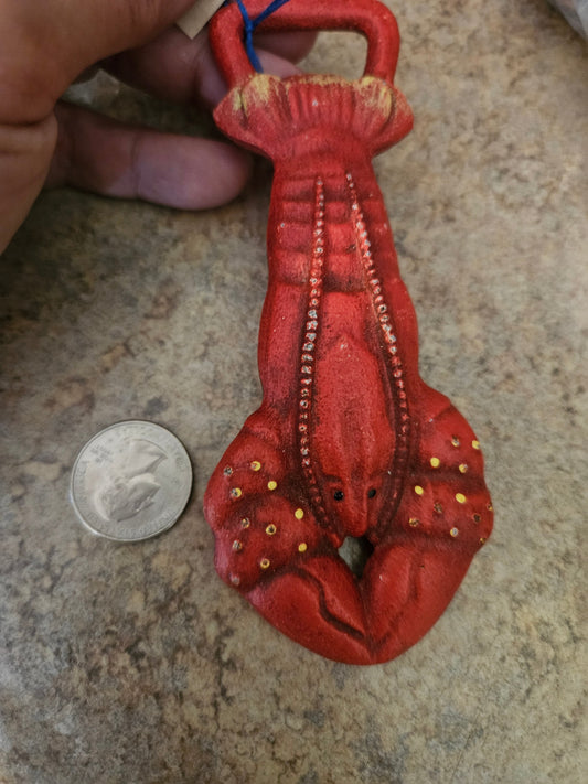 Department 56 cast iron lobster bottle opener in red with gold spot accents, shown with quarter for scale