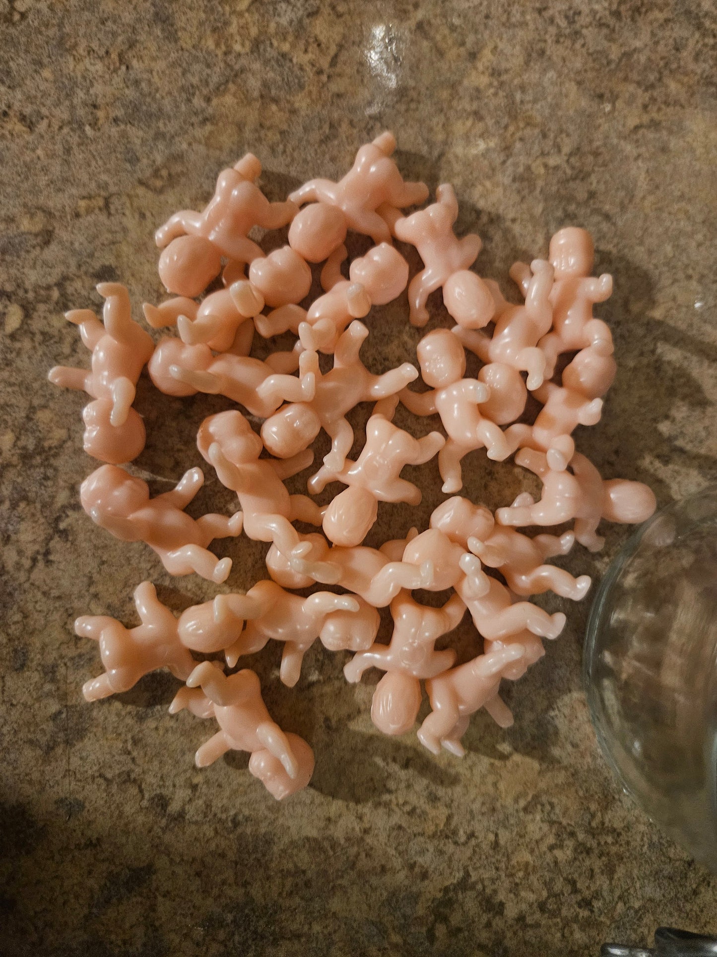 Approximately 40 tiny plastic baby figurines spread out showing size and quantity