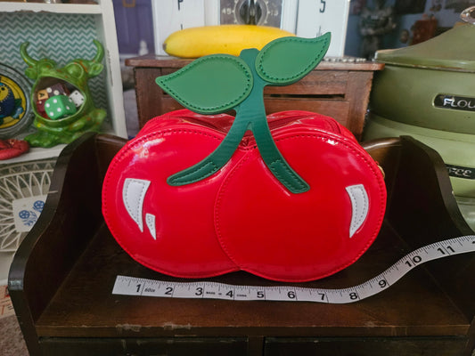 Red patent double-cherry novelty crossbody bag front view showing green leaf stem appliqué and white highlights with ruler for scale