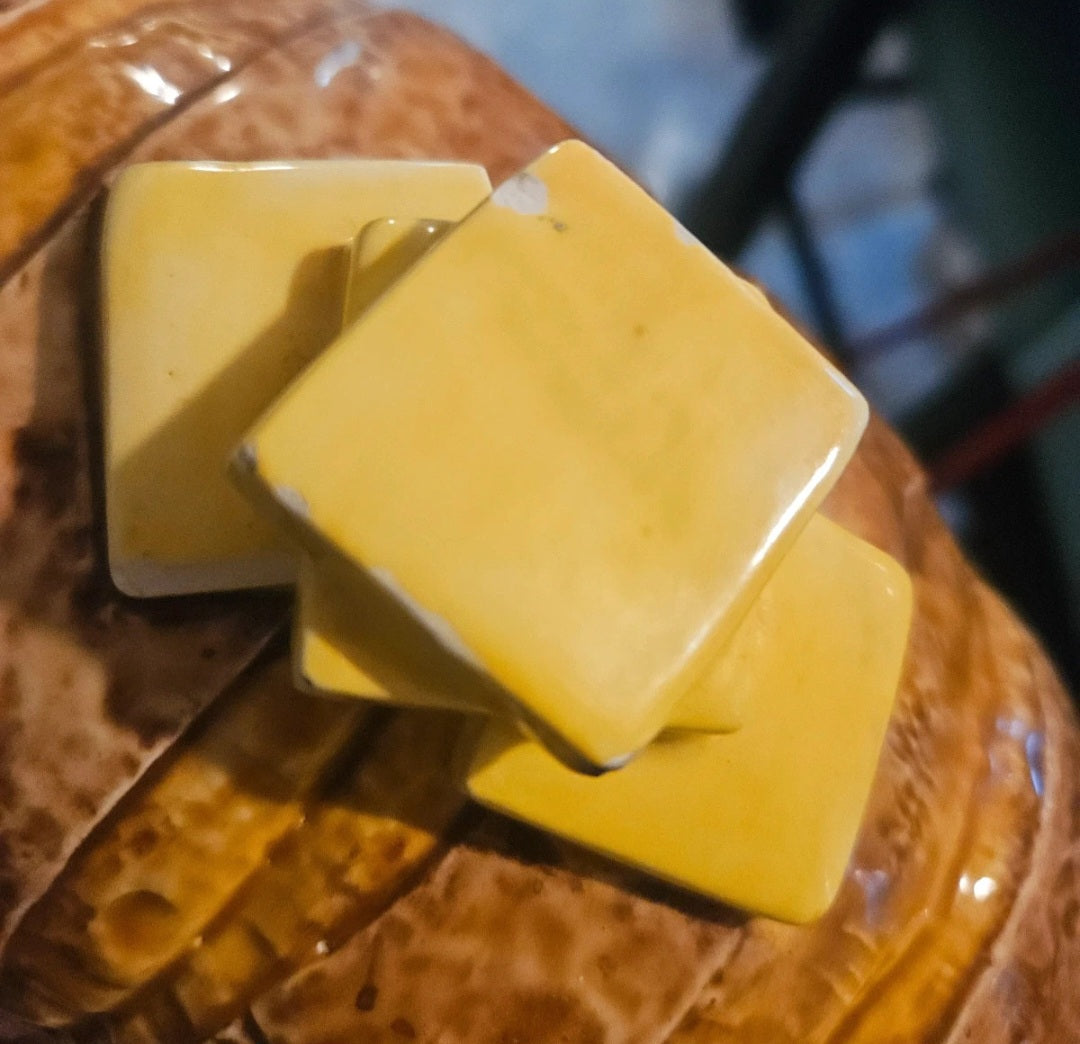 Close up of three stacked yellow ceramic butter pat squares on baked potato cookie jar lid