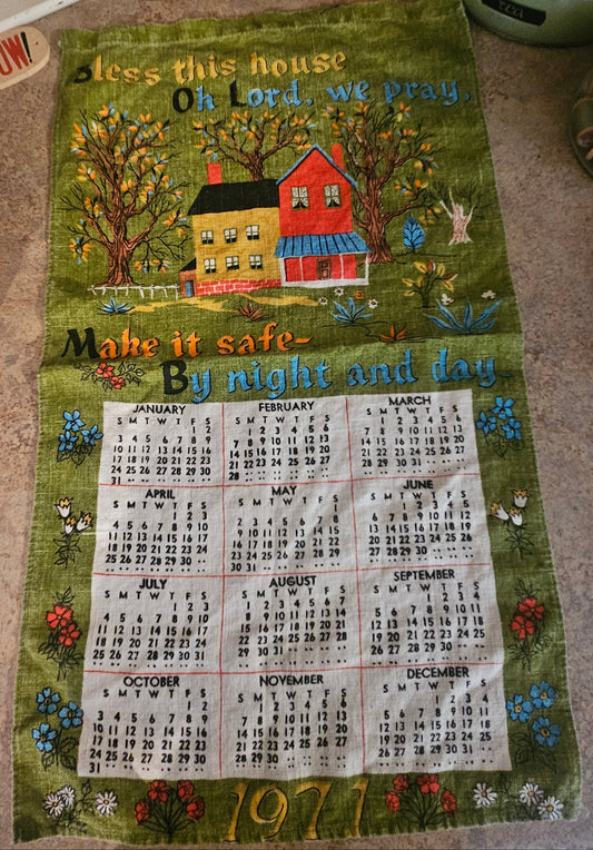 1971 Bless This House calendar tea towel on olive green ground showing folk art farmhouse, autumn trees, and 12-month calendar