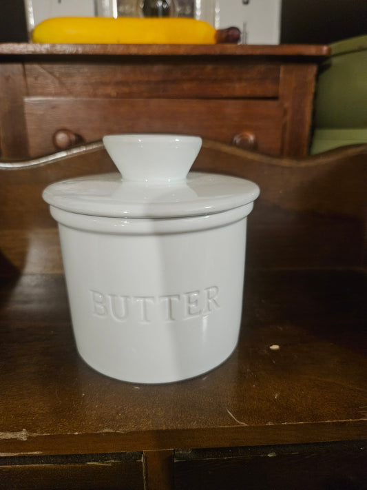 White ceramic French butter bell crock with lid showing embossed BUTTER lettering on exterior