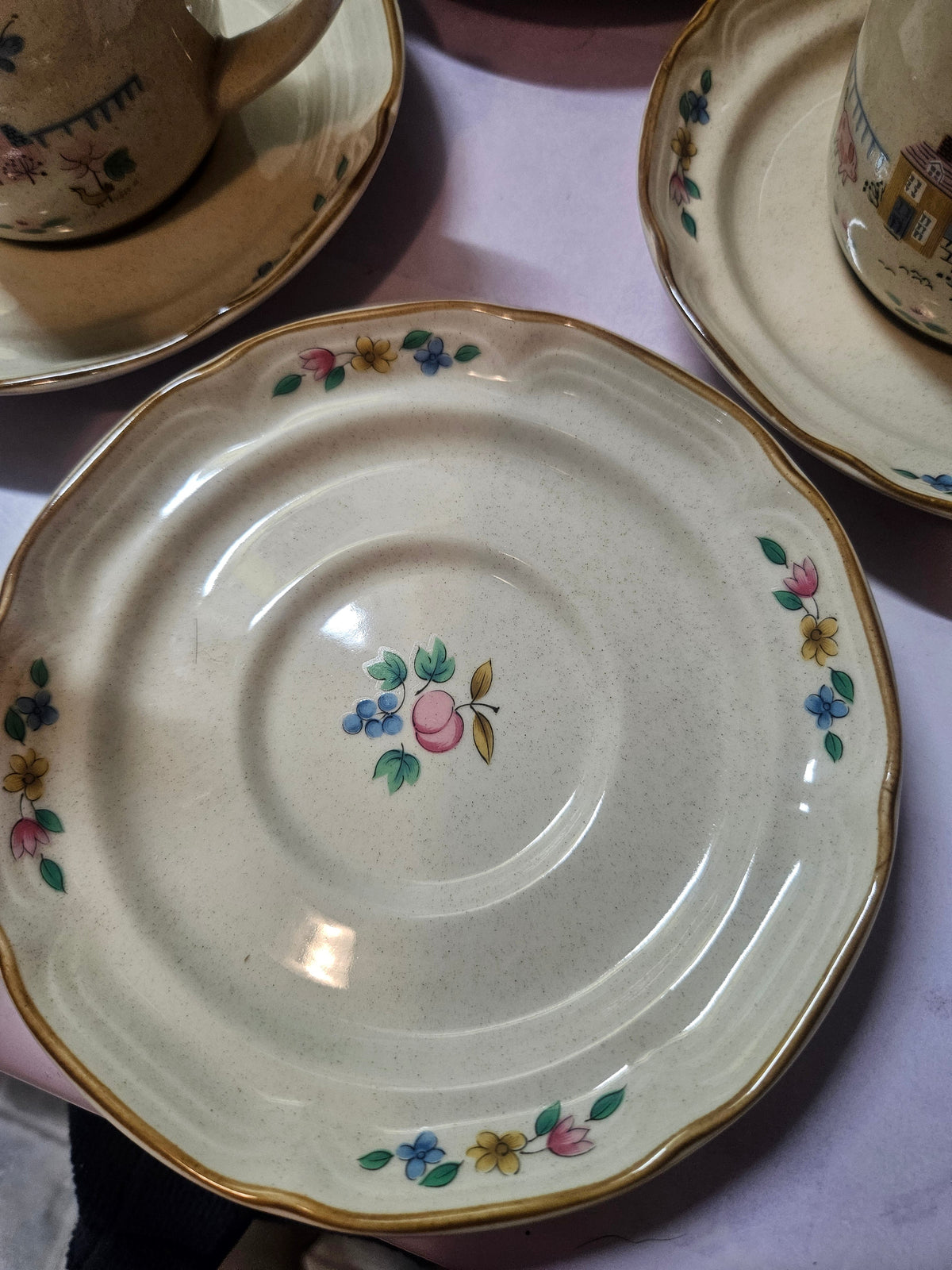 Close-up of a Heartland scalloped saucer with gold trim, speckled cream glaze, and fruit and floral motif