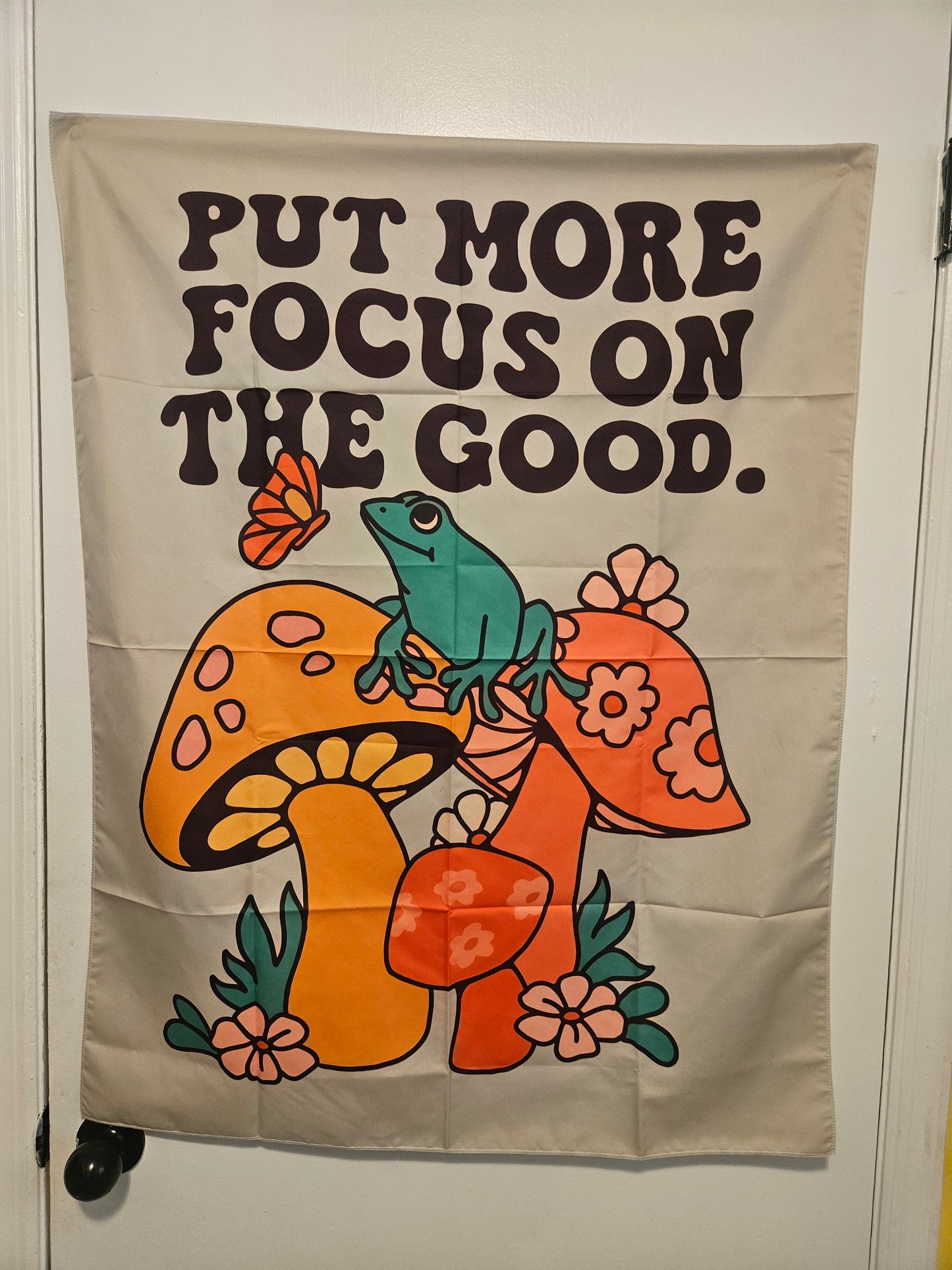 Retro tapestry wall hanging reading Put More Focus on the Good with mushrooms, frog, and flowers