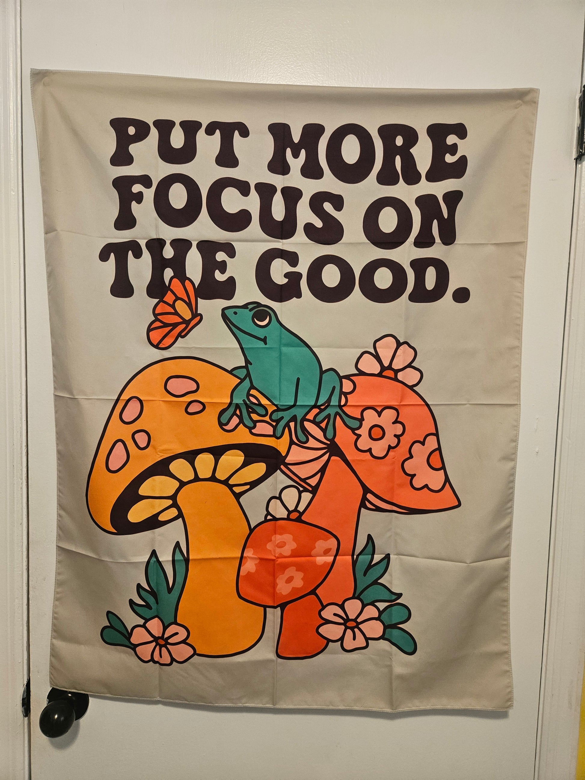 Retro tapestry wall hanging reading Put More Focus on the Good with mushrooms, frog, and flowers