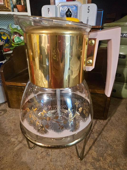 Vintage glass percolator coffee maker front view showing gold floral decoration pink handle gold top and brass warming stand