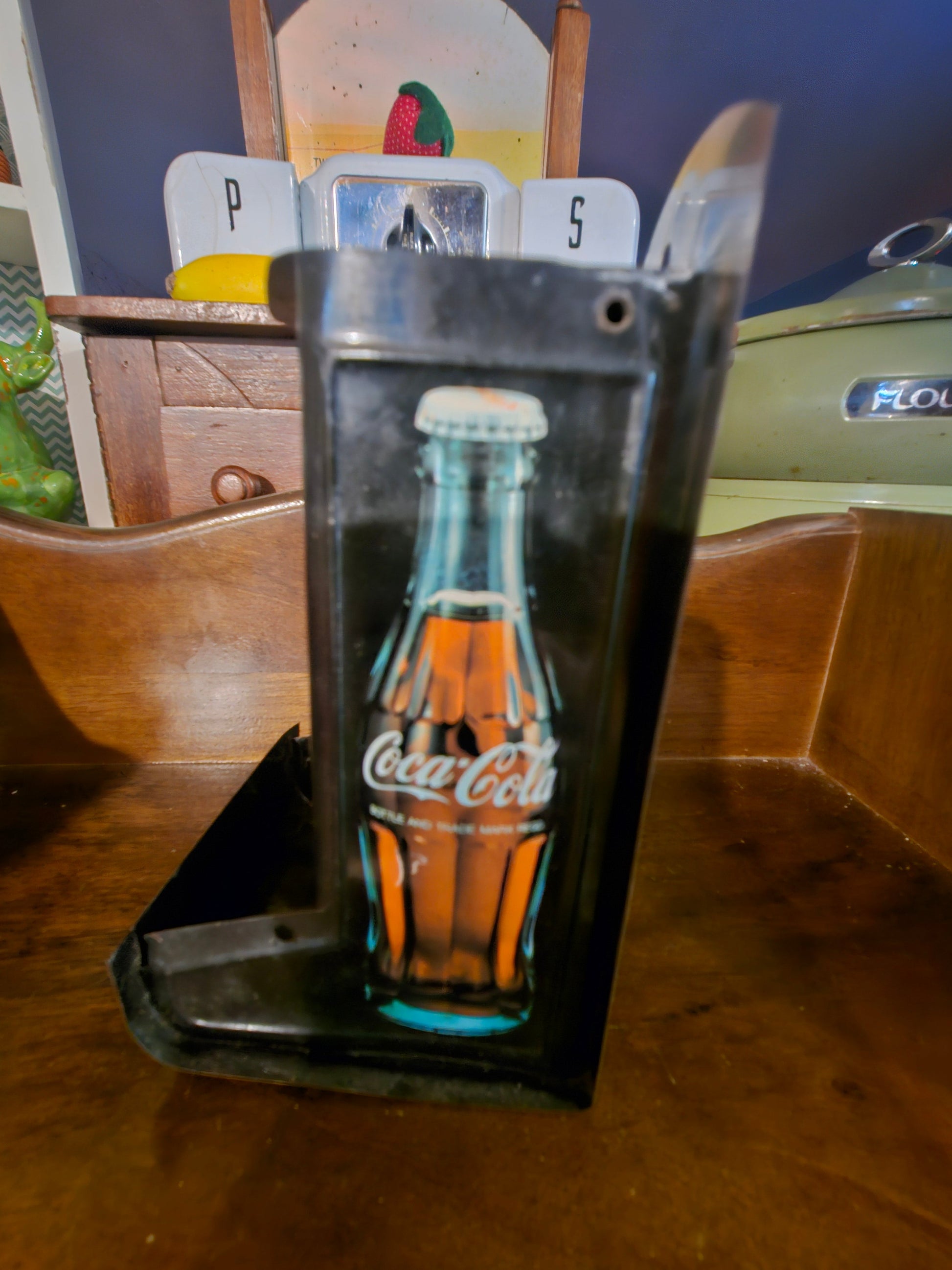 Side of Coca-Cola napkin holder showing contour bottle graphic in teal and orange
