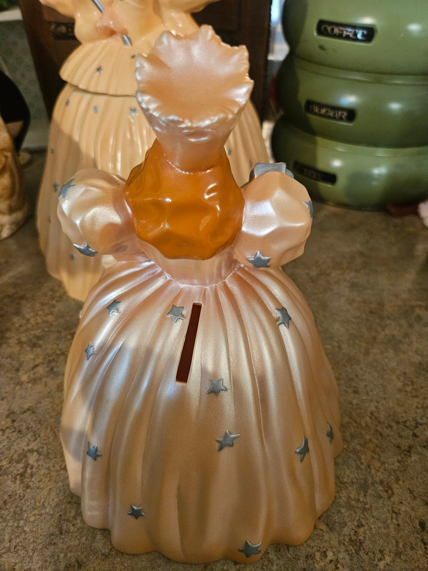 Back view of Glinda coin bank showing coin slot on front skirt and removable head lid