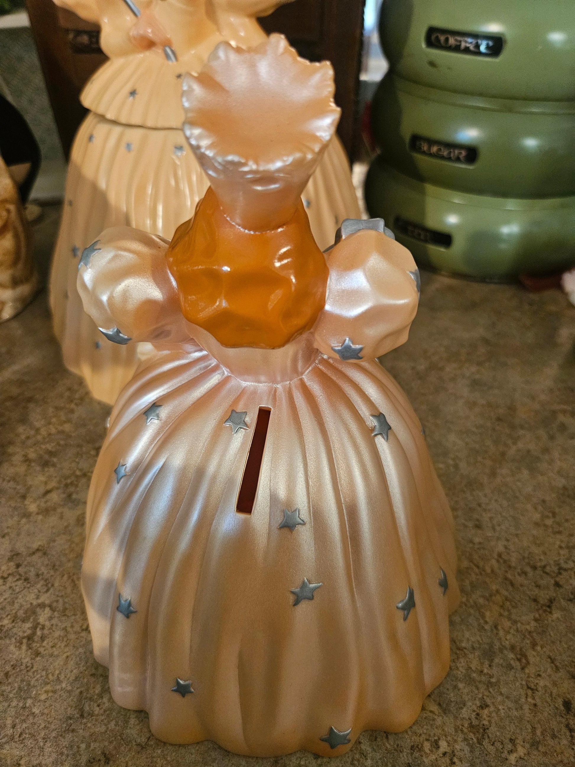 Back view of Glinda coin bank showing coin slot on front skirt and removable head lid
