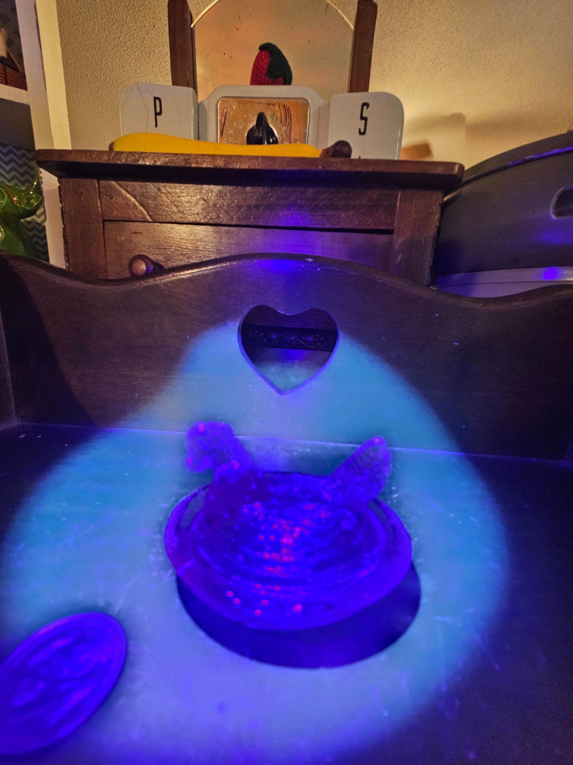 Iridescent carnival glass hen on nest glowing blue and purple under UV blacklight