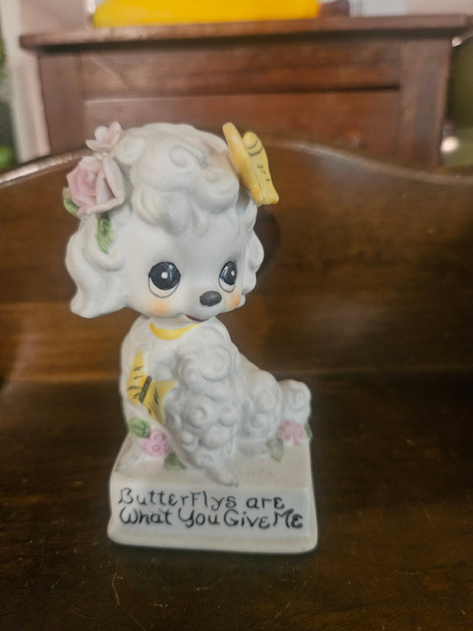 Vintage ceramic poodle figurine front view showing big eyes, yellow butterfly, pink roses, and base inscription