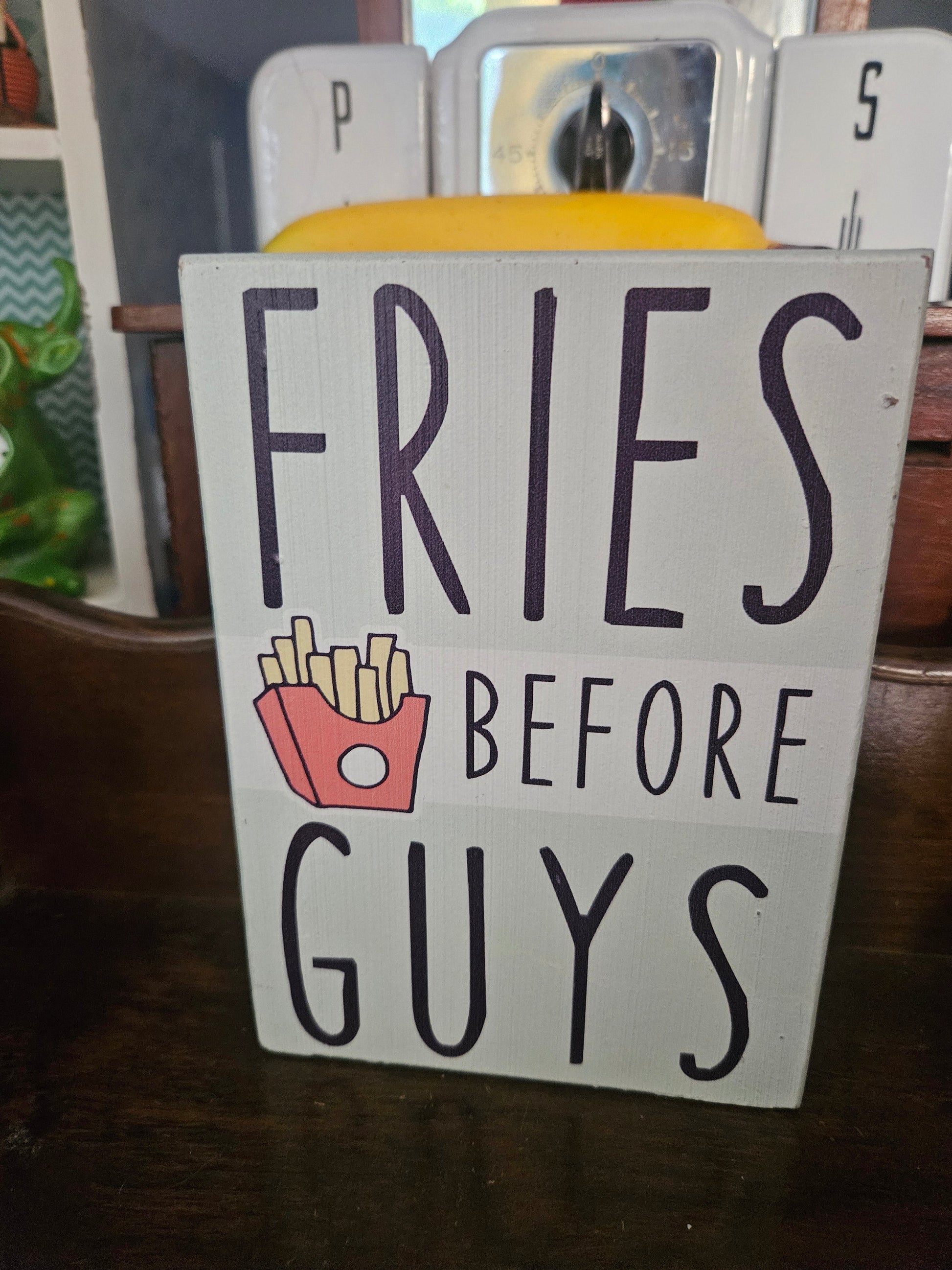 Fries Before Guys white painted wood block sign with black hand-lettered text and french fry illustration, front view