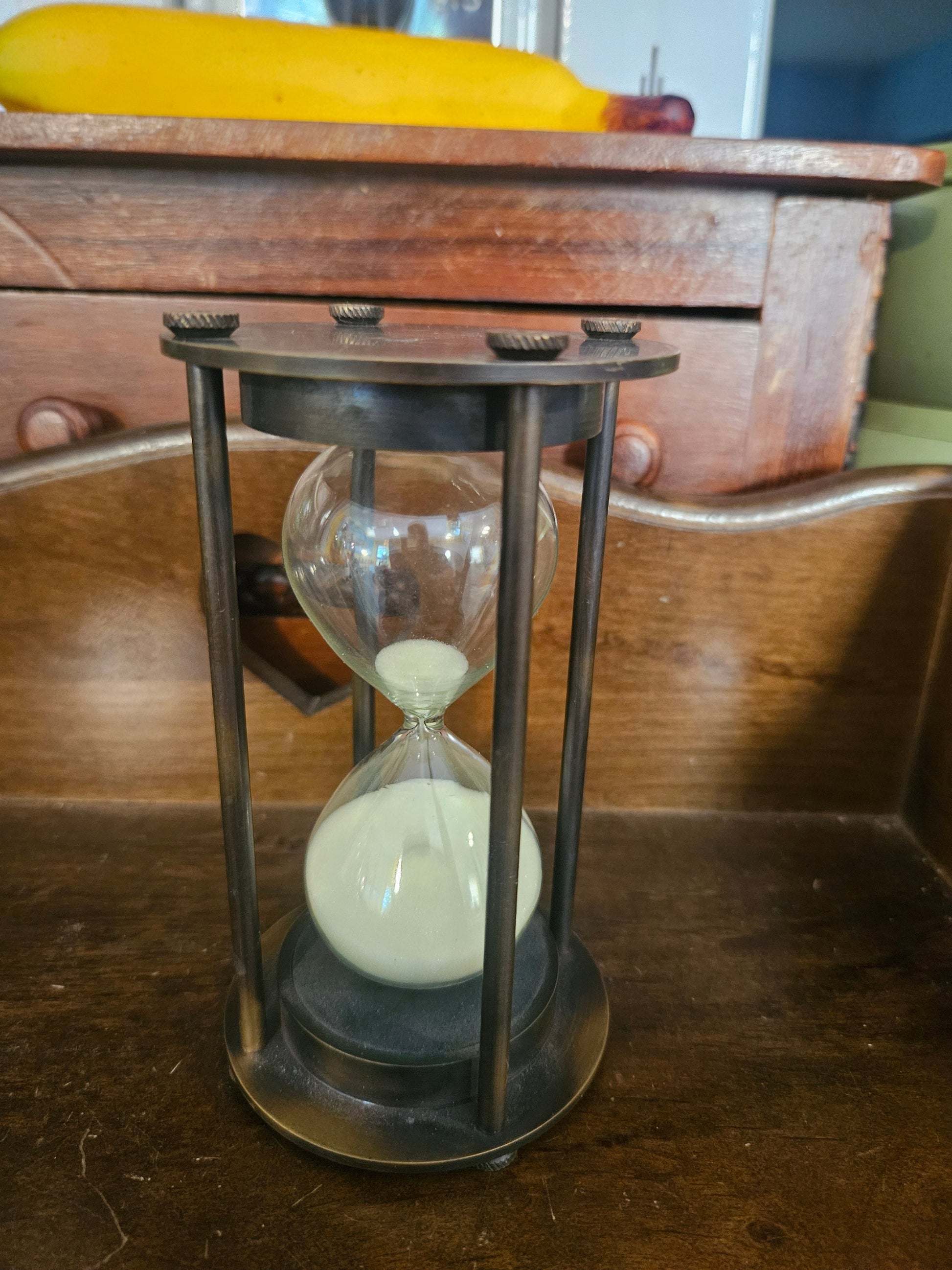 Vintage brass hourglass sand timer with four-post frame and gear-style knurled knobs showing white sand and aged patina