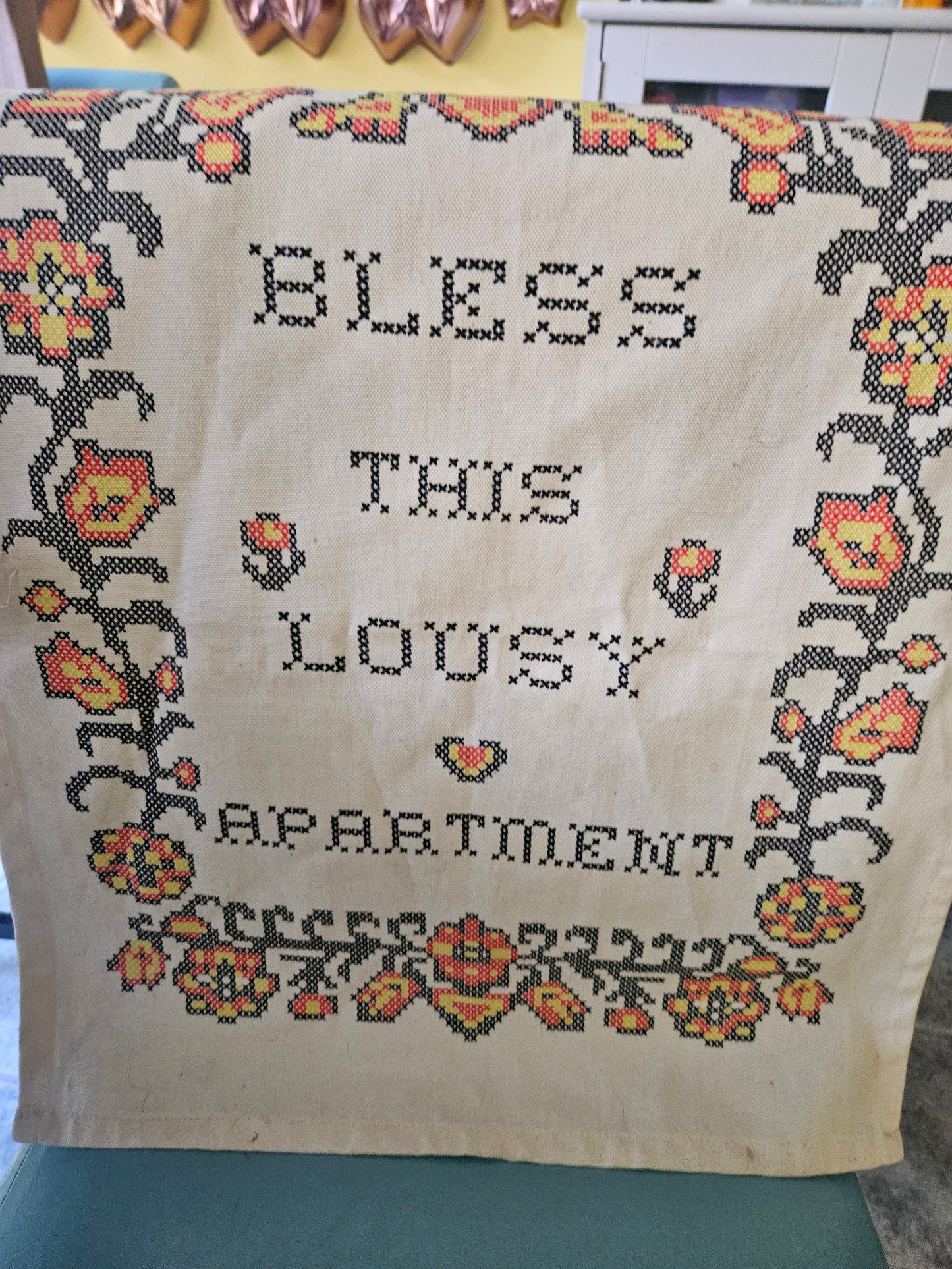 Bless This Lousy Apartment cross-stitch style wall hanging front view showing folk floral border and block lettering