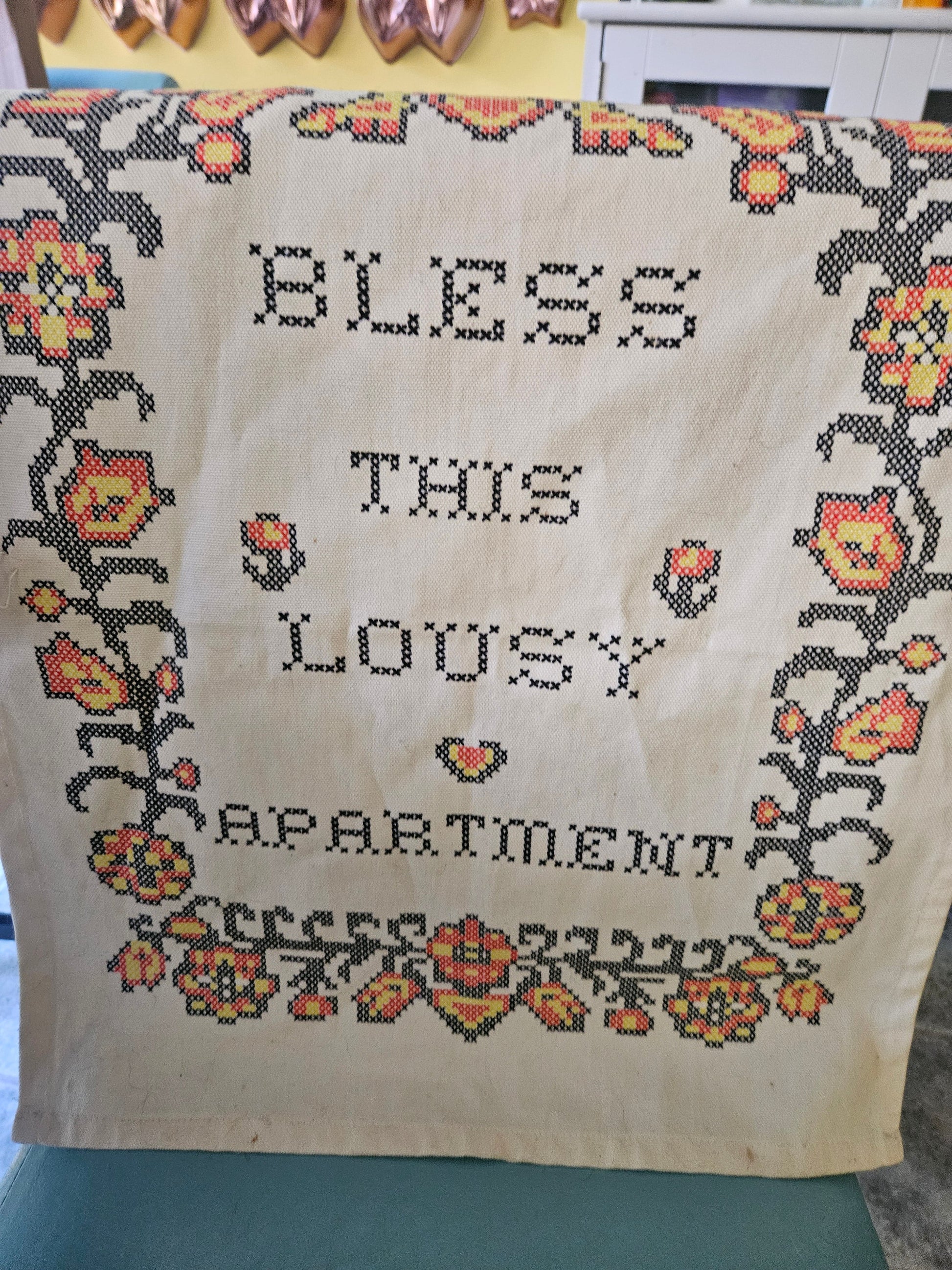 Bless This Lousy Apartment cross-stitch style wall hanging front view showing folk floral border and block lettering