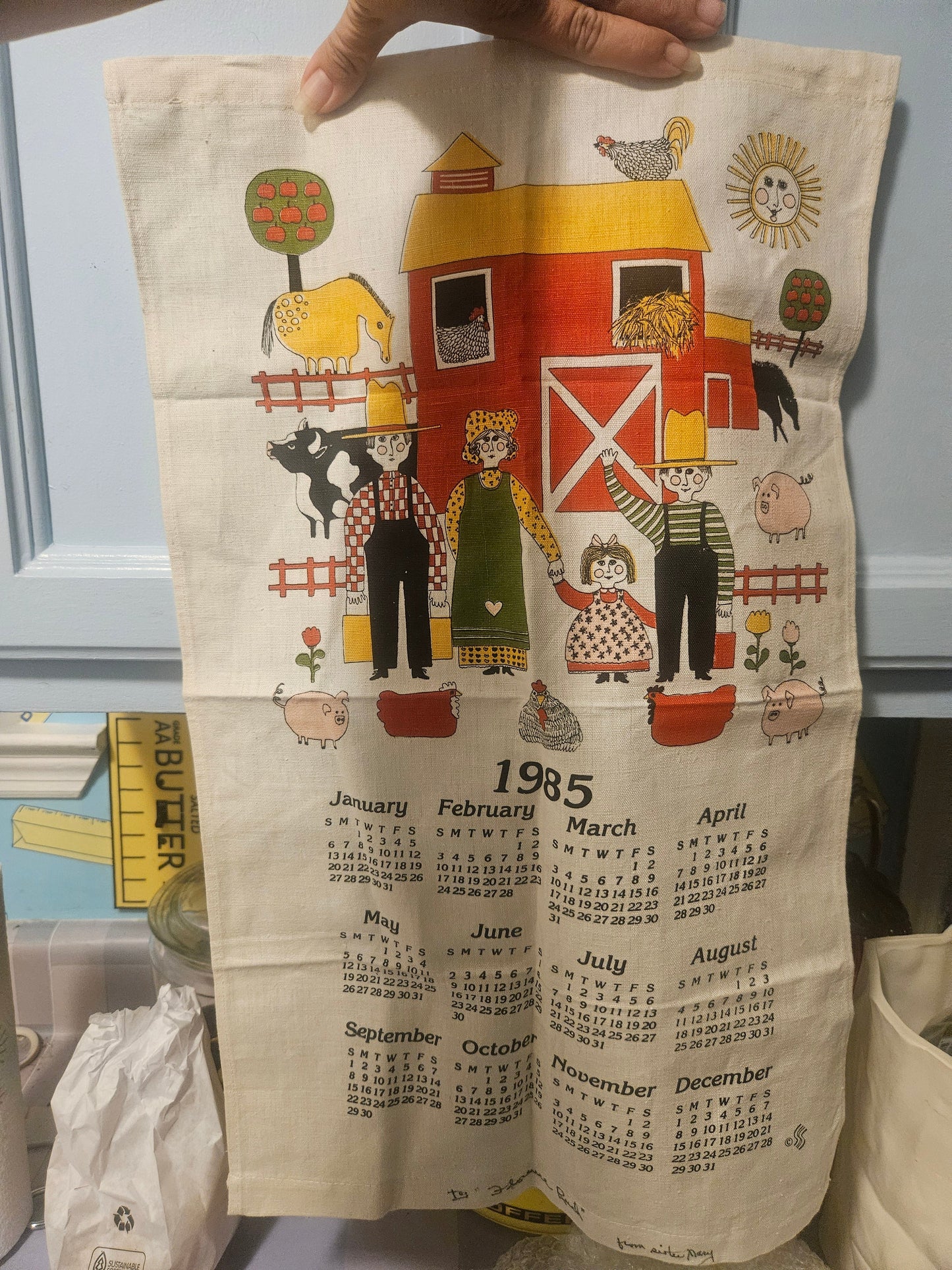 1985 linen calendar tea towel with folk art farm scene showing barn, farmers, animals and full year calendar