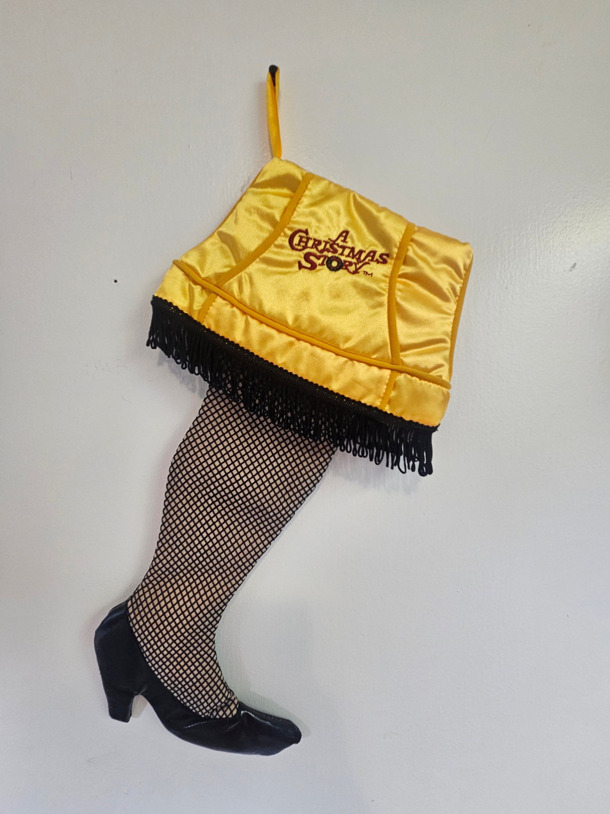 A Christmas Story Leg Lamp Christmas stocking front view showing gold satin shade with embroidered logo, black fringe, fishnet leg and black heel