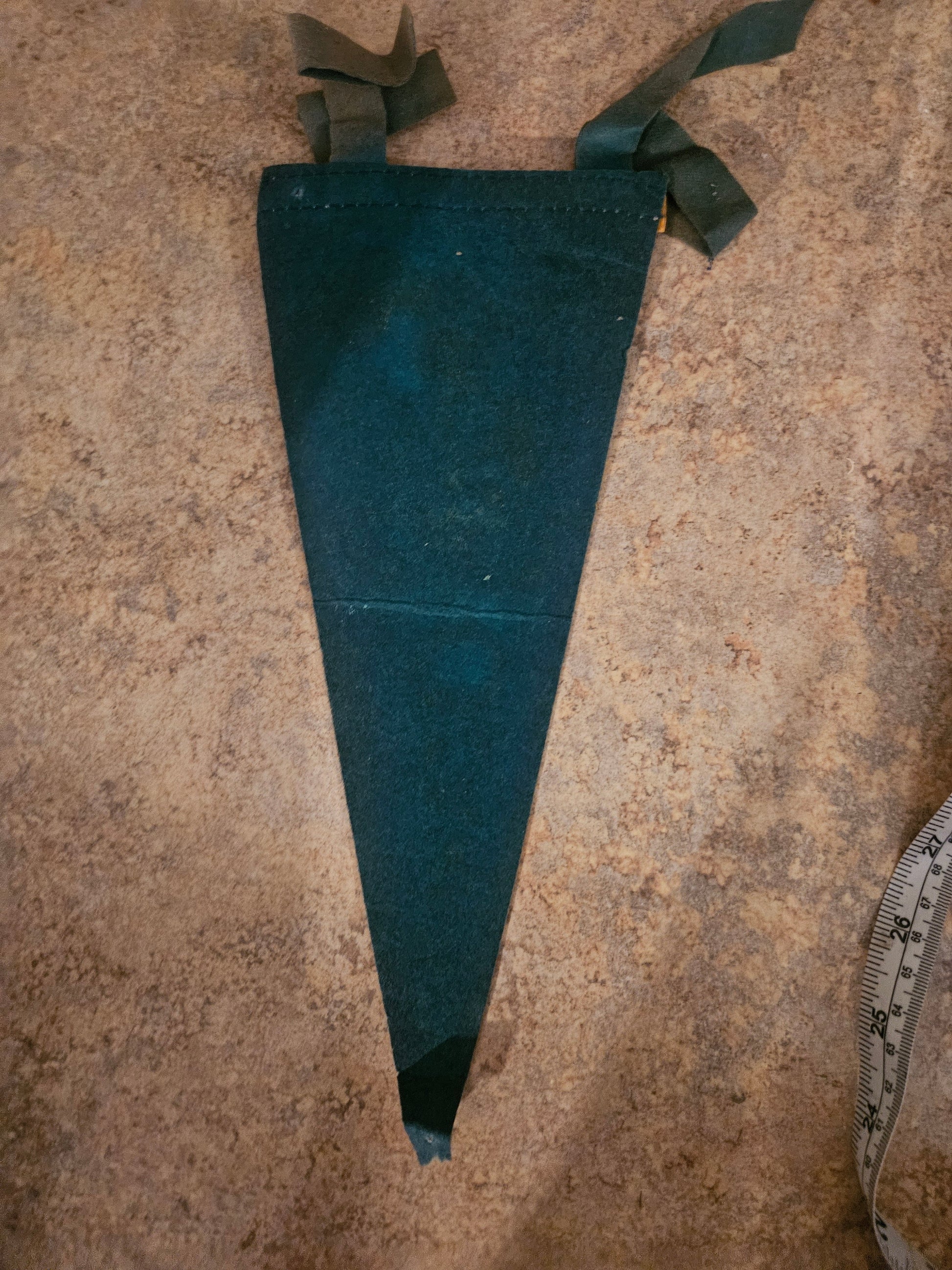 Back of vintage Ozarks felt pennant showing green ribbon ties and gold leather trim band with ruler for scale