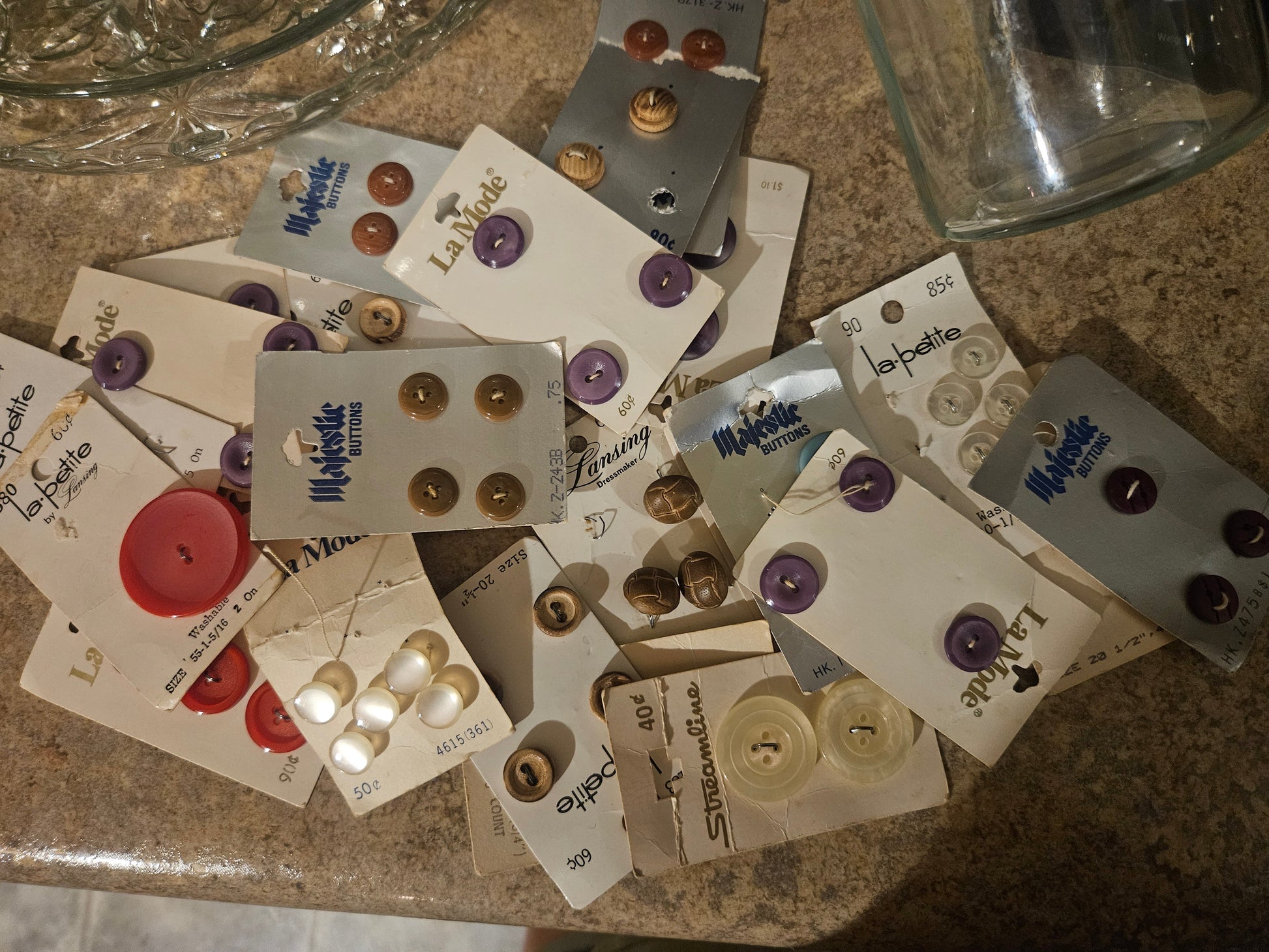 Vintage button cards spread out showing La Mode, Majestic, La Petite, and Streamline brands in purple, red, pearl, and gold