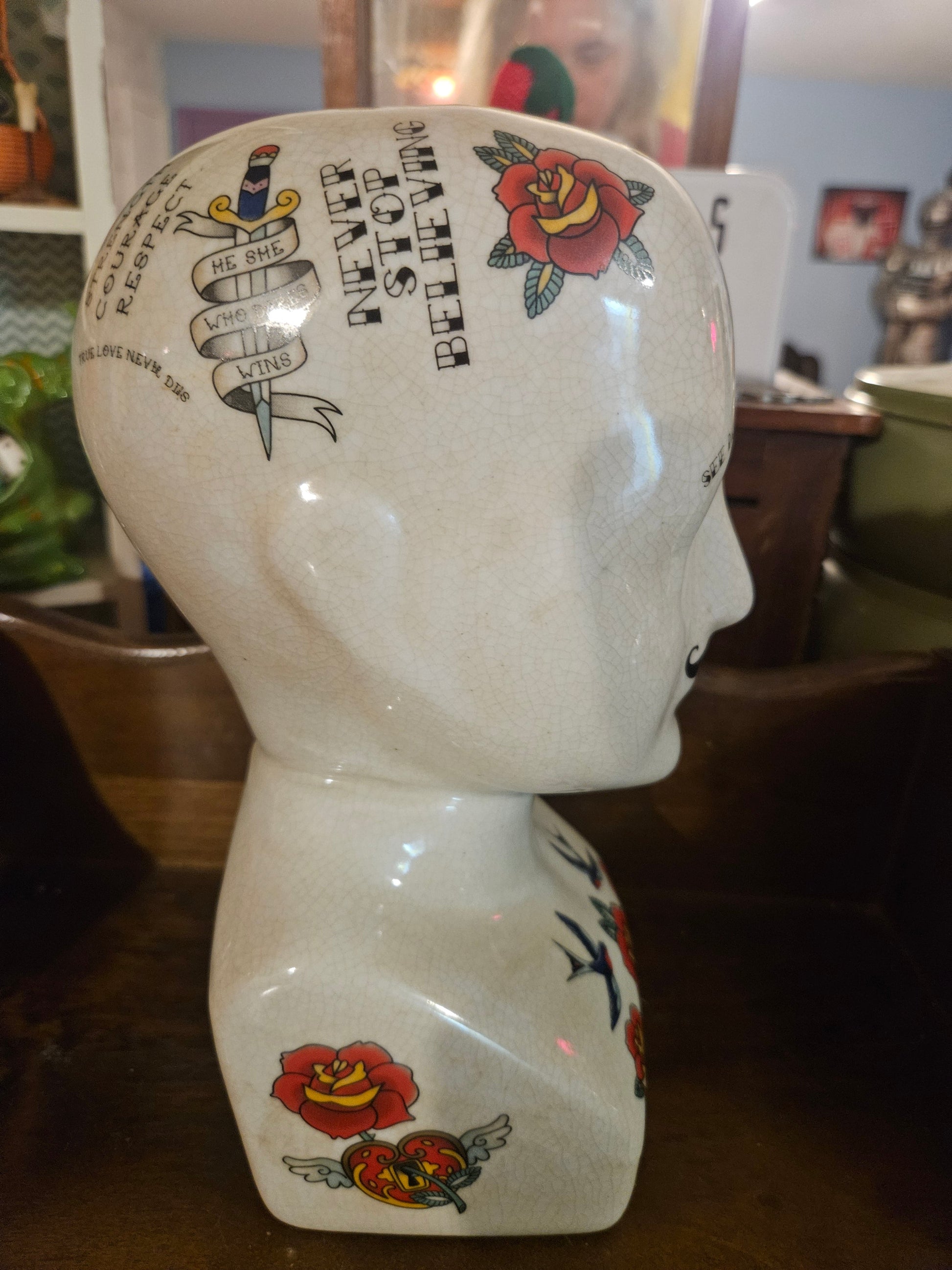 Side view of ceramic phrenology head planter showing Never Stop Believing text roses and tattoo flash art
