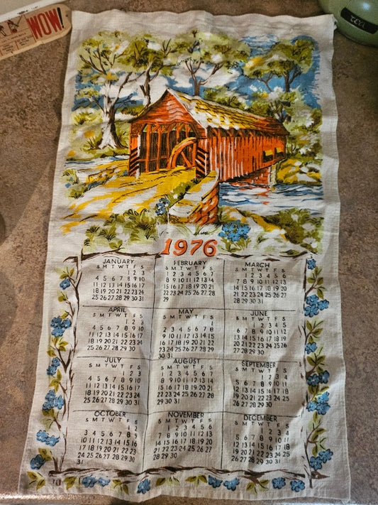 1976 covered bridge calendar tea towel showing full-color scene with waterwheel, forget-me-nots, and 12-month calendar
